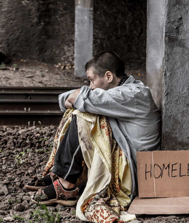 A homeless young man sits under a bridge with a cardboard sign.