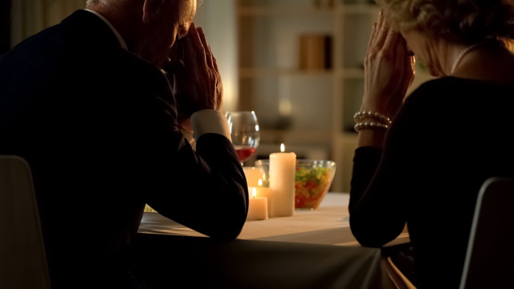 Man and woman sitting at a candlelit table with their heads in their hands