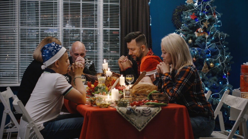 Family of five saying grace at the dinner table during Christmastime