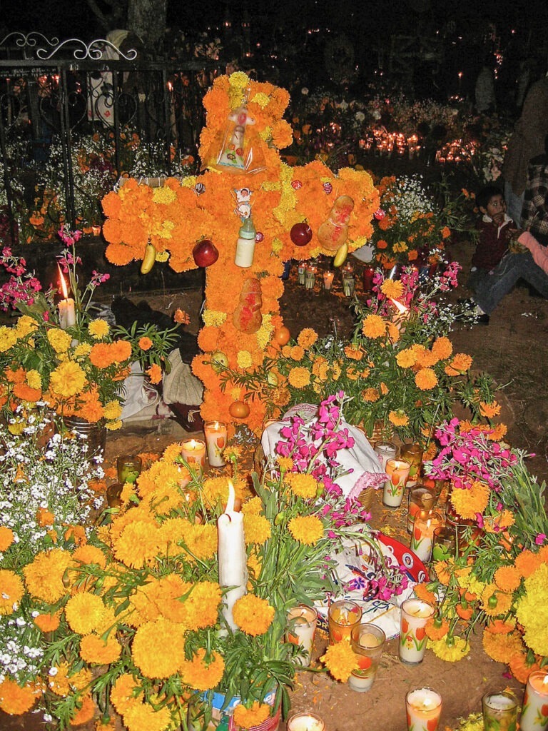 An altar made of flowers in the shape of a cross with mementos, flowers and other gifts made of a Day of the Dead celebration.