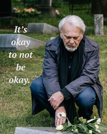 older man placing flowers at a gravestone.