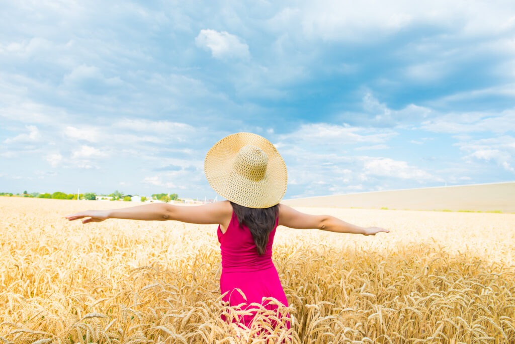 Woman in hat with outstretched arms in a wheat field