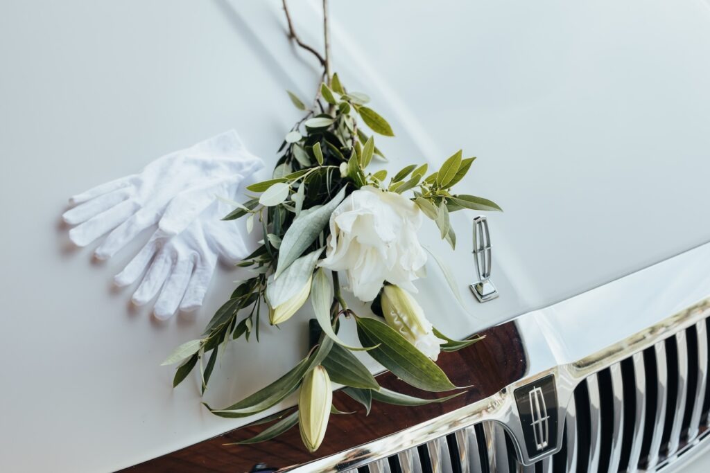 Flowers and white gloves sitting on the hood of a white hearse.