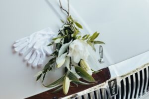 Flowers and white gloves sitting on the hood of a white hearse.