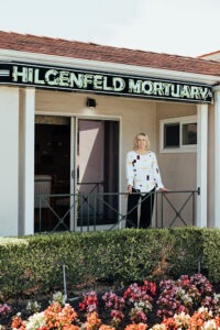 Woman stands under neon Hilgenfeld Mortuary sign
